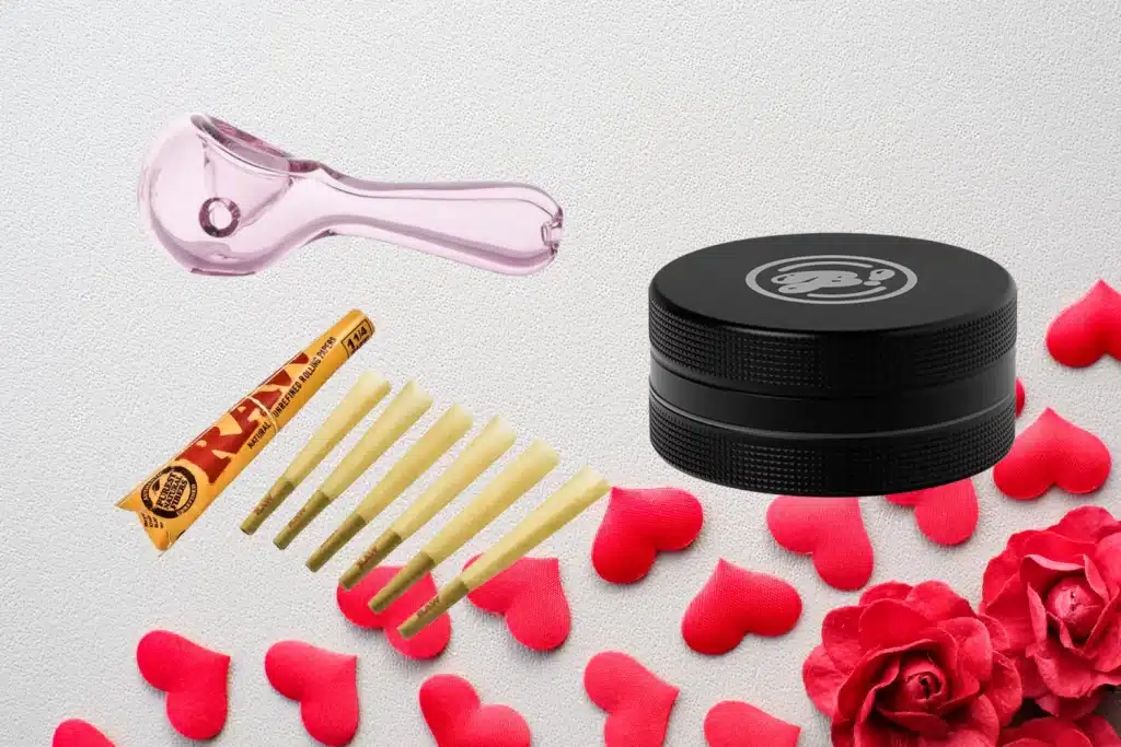 A romantic Weed Valentines Gift display featuring smoking essentials, including a pink glass pipe, a black grinder, RAW pre-rolled cones, and rolling papers. The items are arranged on a soft background with red hearts and roses, creating the perfect cannabis-themed Valentines Day Gift.