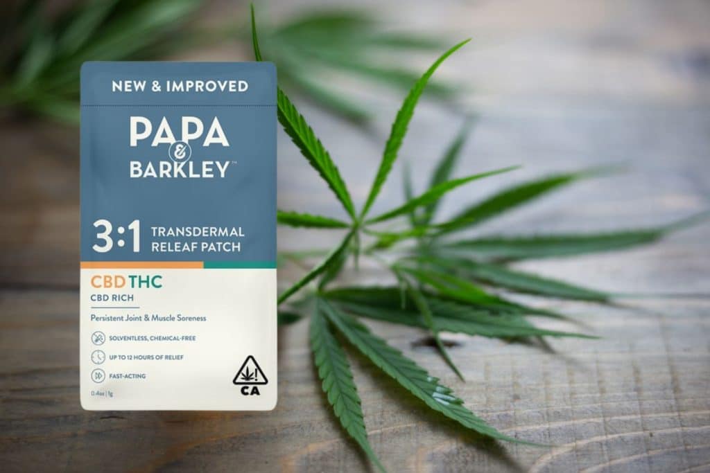 Papa & Barkley 3:1 CBD THC transdermal releaf patch standing against a wooden surface with fresh cannabis leaves in the background.