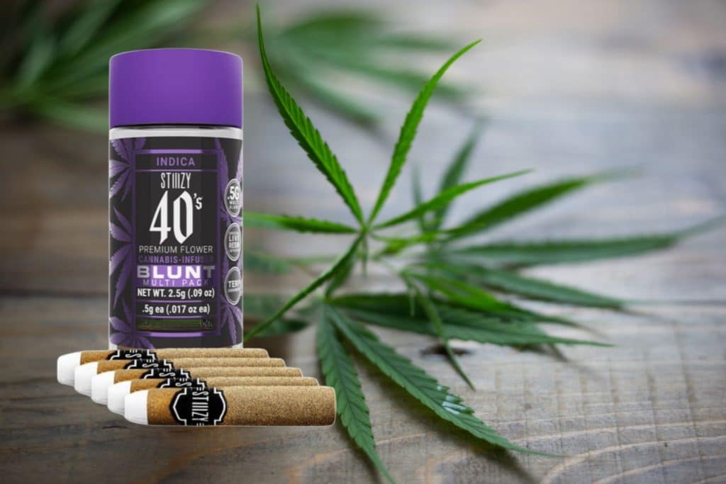 Stiiizy 40s Indica blunt multipack with a purple cannabis-infused flower container and pre-rolled blunts, placed on a wooden surface with cannabis leaves around.